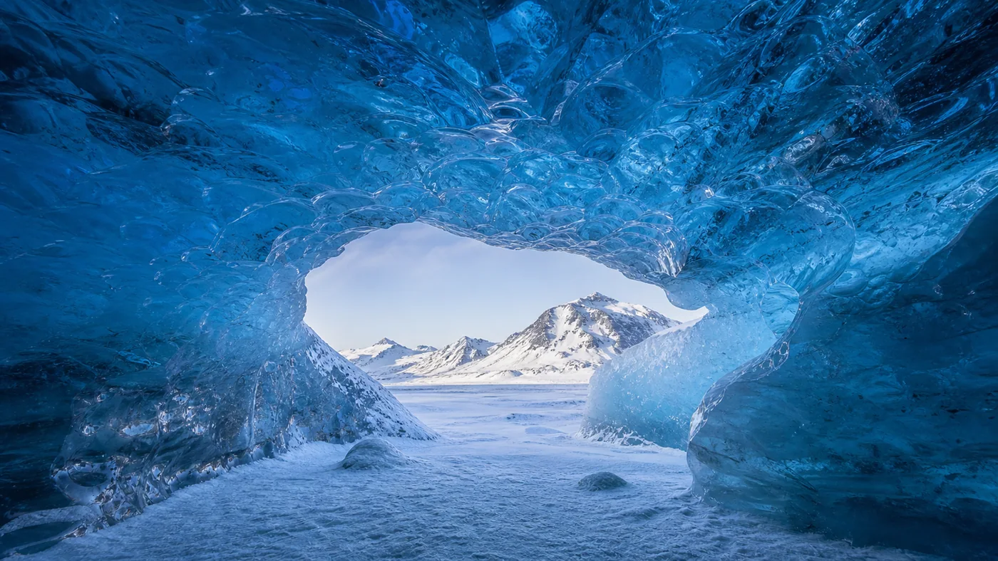Blue Ice Chapel — Translucent sapphire ice frames white snow and distant mountains with sacred quiet.