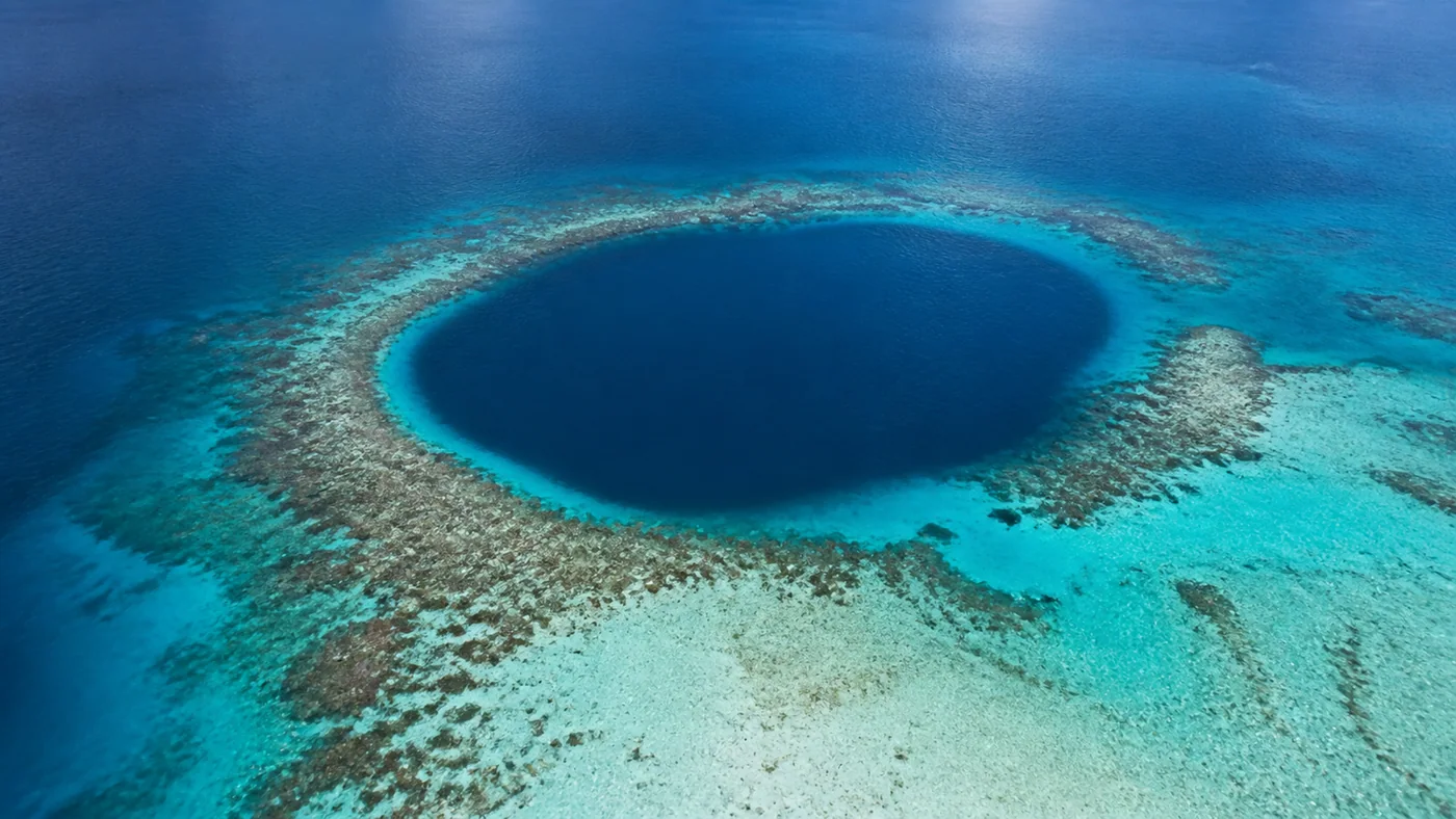 Blue Hole Clarity — Deep navy water, turquoise reef, and ivory sand create a quiet visual shock.
