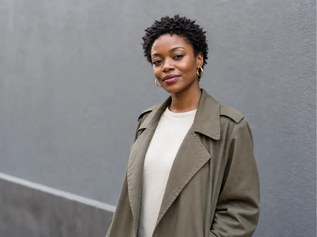 Source portrait: a woman in an olive trench coat in front of a plain gray wall